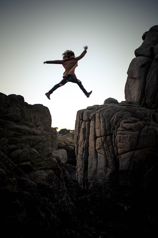 Eine Person springt auf einen Felsen, Foto von Sammie Chaffin (https://unsplash.com/@sammiechaffin) auf Unsplash (https://unsplash.com/photos/Zdf3zn5XXtU)